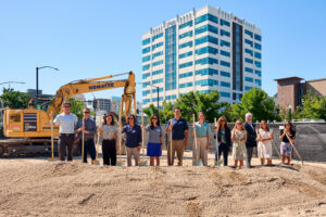 A group of people stand on a dirt mound with shovels for a groundbreaking ceremony